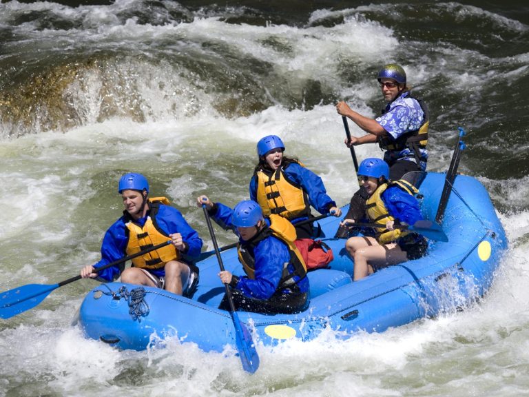 Groupe de cinq personnes faisant du rafting sur une rivière tumultueuse.